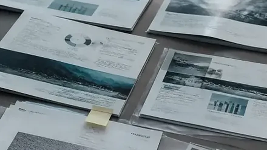 A hand marking a printed sheet among prints spread over a desk